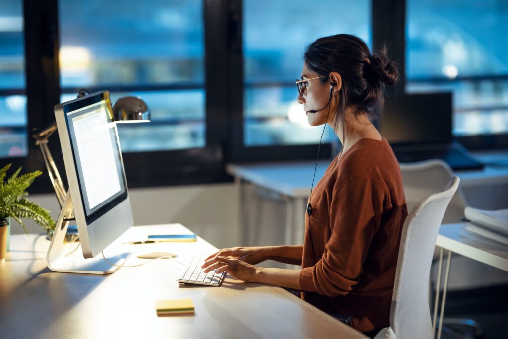 Beautiful business woman working with computer while talking with earphone sitting in the office.