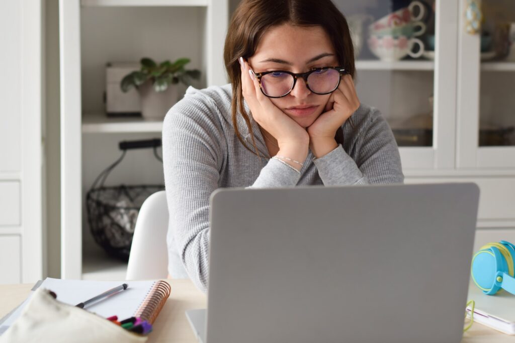 Young teenage girl sitting bored while studying in front of laptop computer